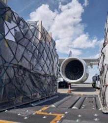 Preparation before flight. Loading of cargo containers against jet engine of freight airplane.